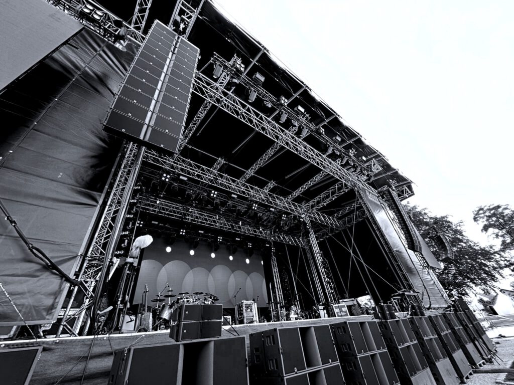 Frontalaufnahme einer professionellen Eventbühne, perfekt ausgeleuchtet und bereit für den Einsatz. Erkennbar sind Scheinwerfer, Traversen und Beschallungsanlagen