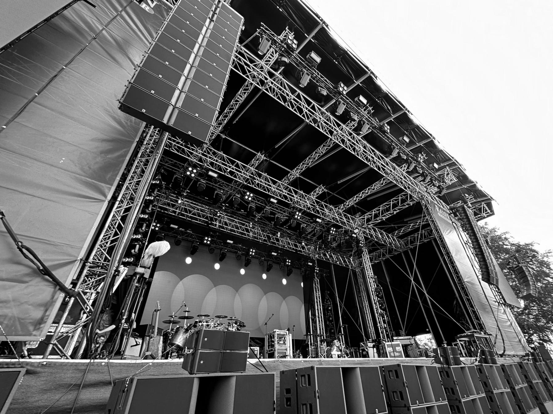 Frontalaufnahme einer professionellen Eventbühne, perfekt ausgeleuchtet und bereit für den Einsatz. Erkennbar sind Scheinwerfer, Traversen und Beschallungsanlagen